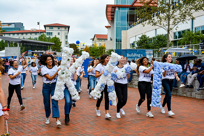 Members of a sorority walk through the parade, holding Greek letters